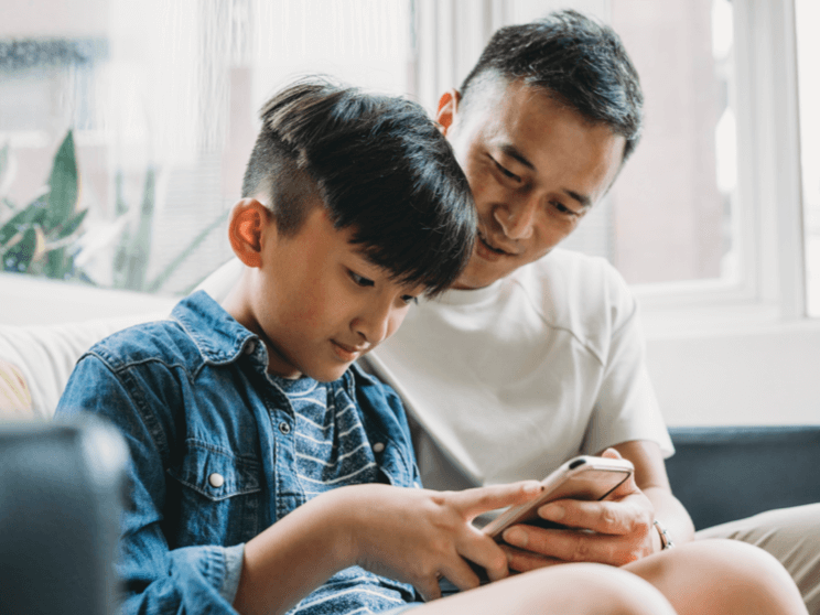 Father and son using a mobile phone together sitting on the sofa at home