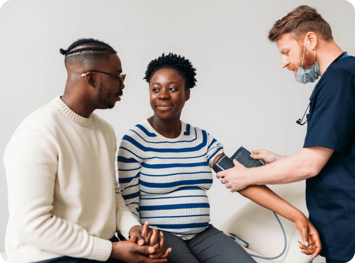 Beautiful young pregnant woman and her life partner having regular checkup with their doctor. Medical doctor measuring blood pressure of pregnant woman